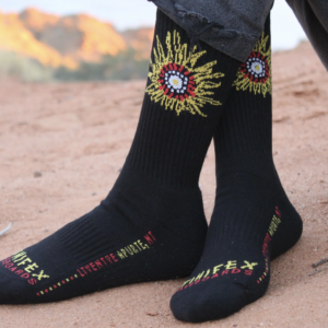 Black, crew cut socks being worn on desert sand - The Spinifex Skate logo is embroidered at the top, and the brand name is written in text across the toe.